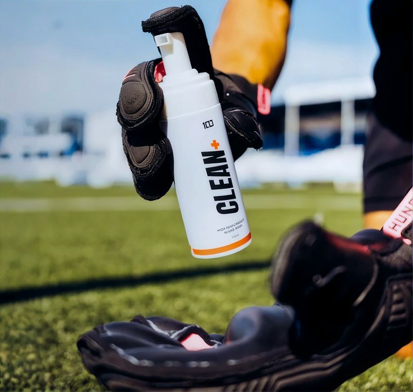 Hundred Clean+ glove wash held in front of a pair of goalkeeper gloves
