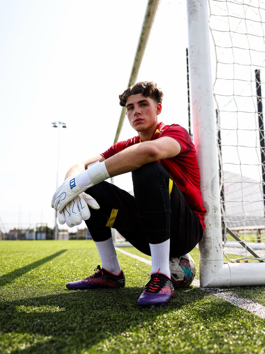 Young goalkeeper in Hundred gloves sitting by the goal