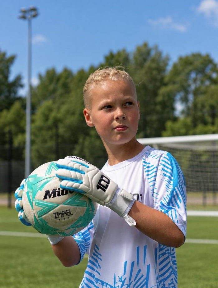 Junior goalkeeper holding a ball in Hundred kit