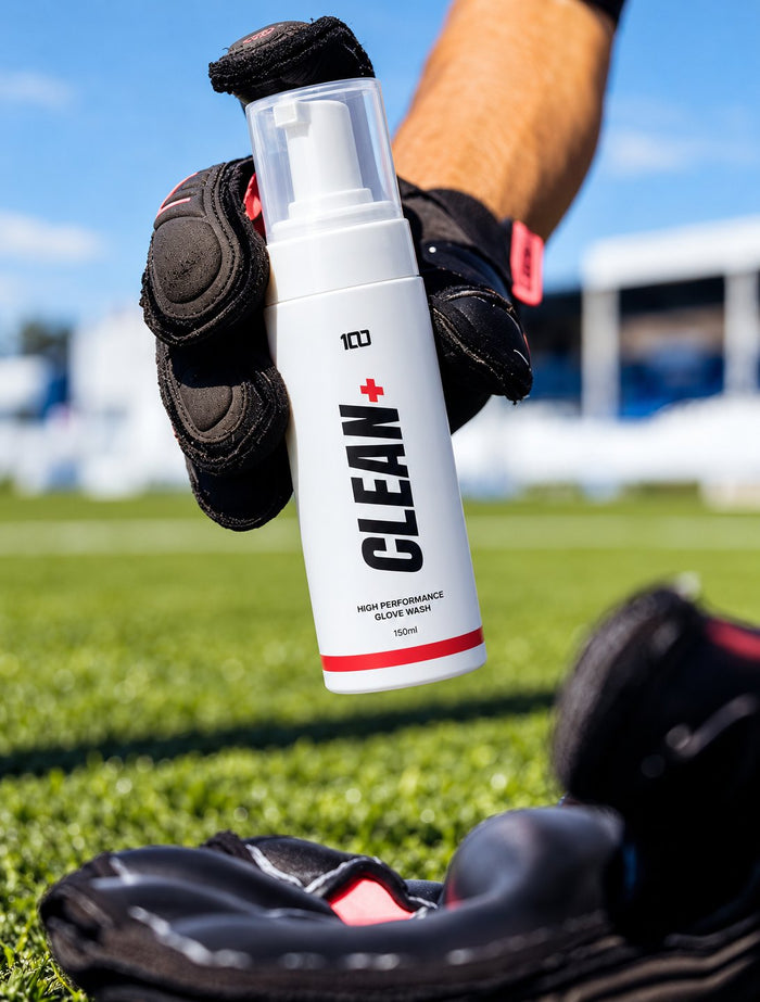 Hundred Clean+ glove wash held above a pair of goalkeeper gloves